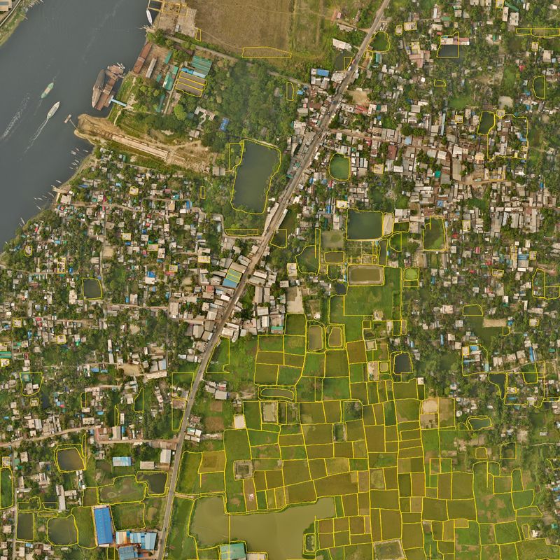 One square kilometre of Narayanganj seen from the air, with the field edges our model drew in yellow. Paddy fields in the south are outlined one by one, while the town in the north has only scattered outlines.