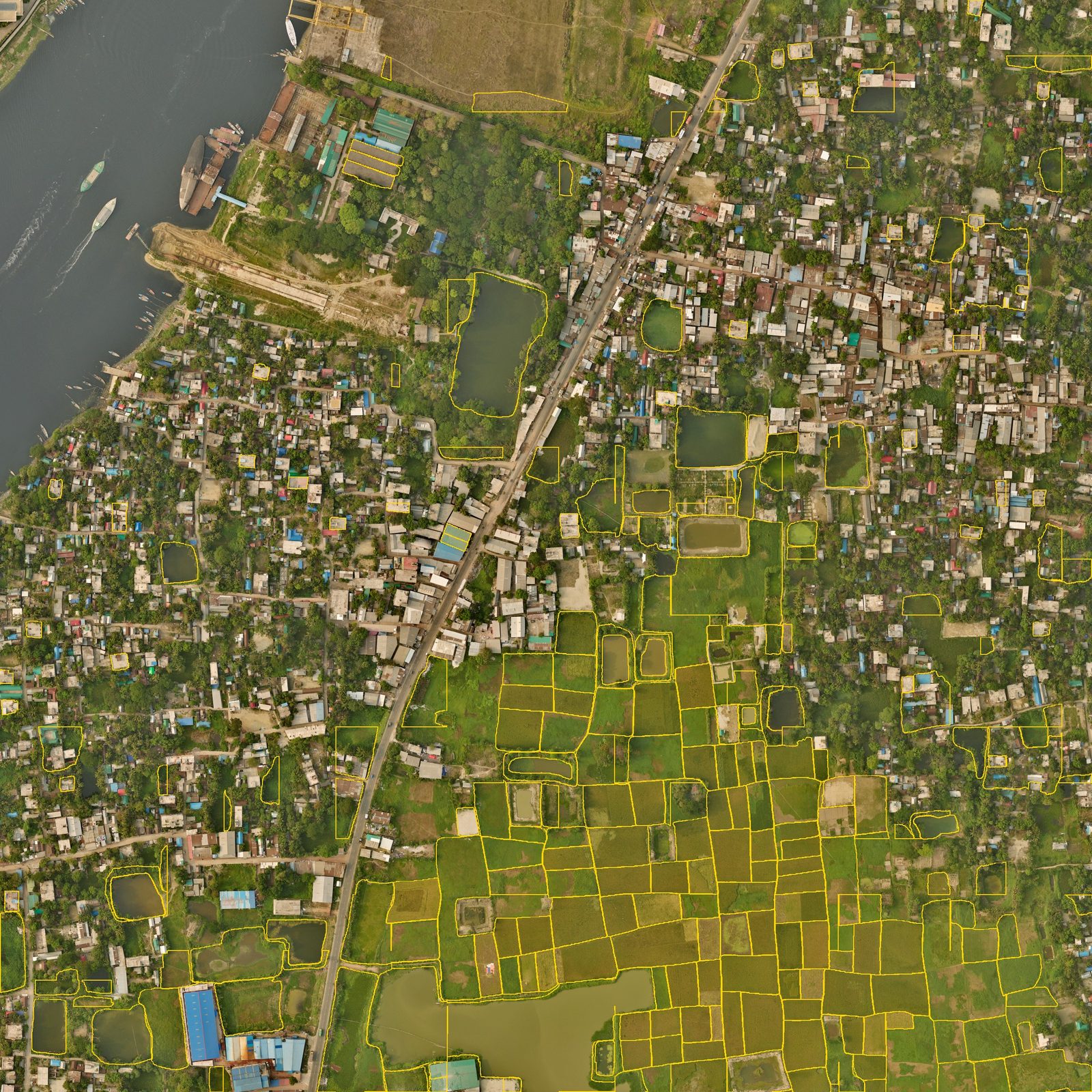 One square kilometre of Narayanganj seen from the air, with the field edges our model drew in yellow. Paddy fields in the south are outlined one by one, while the town in the north has only scattered outlines.
